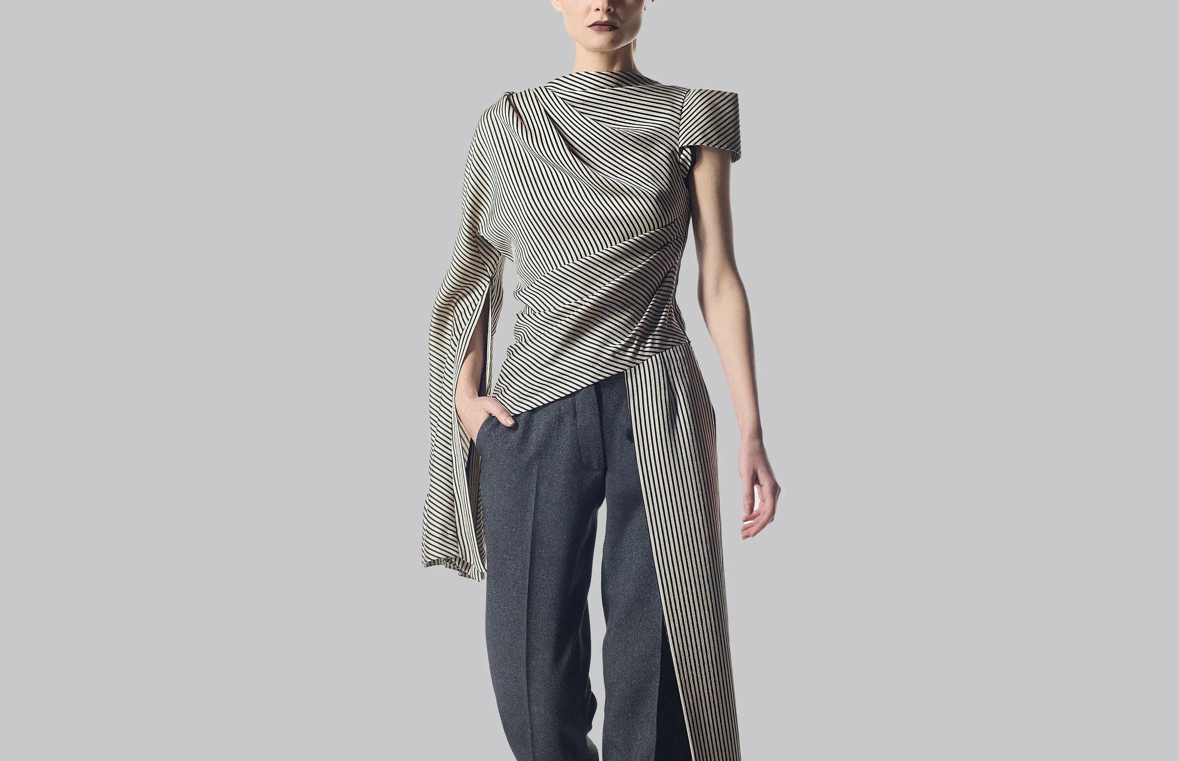 Striped cold-shoulder button-down shirt with gray trousers.