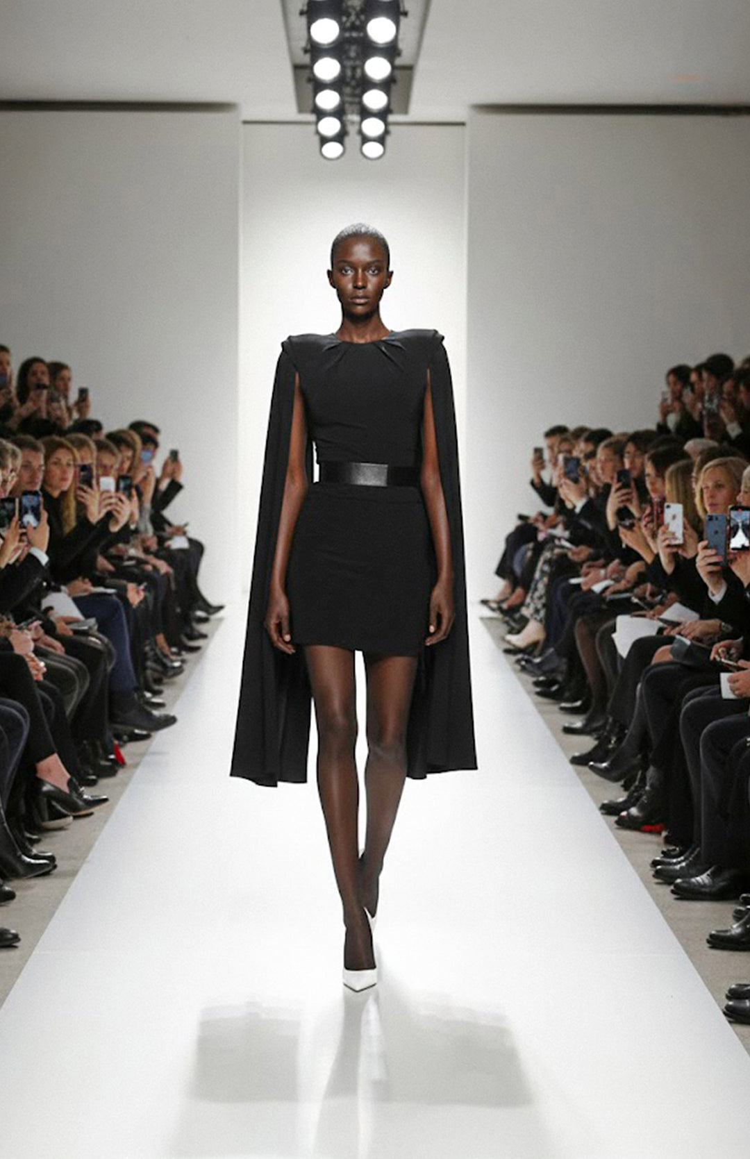 model is wearing mini black dress with cape sleeves on the runway