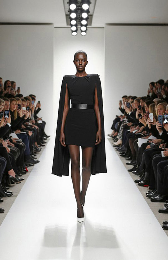 model is wearing mini black dress with cape sleeves on the runway