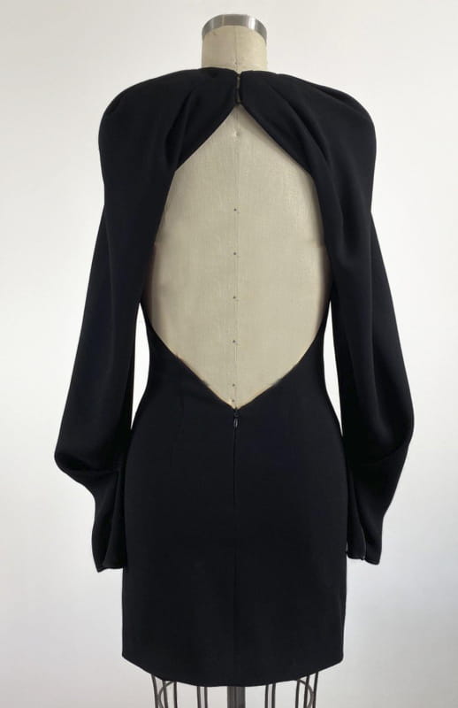 A one-off piece and the perfect little black dress. This is a short backless style with oversized draped sleeves and closed neck with pleated detailing.