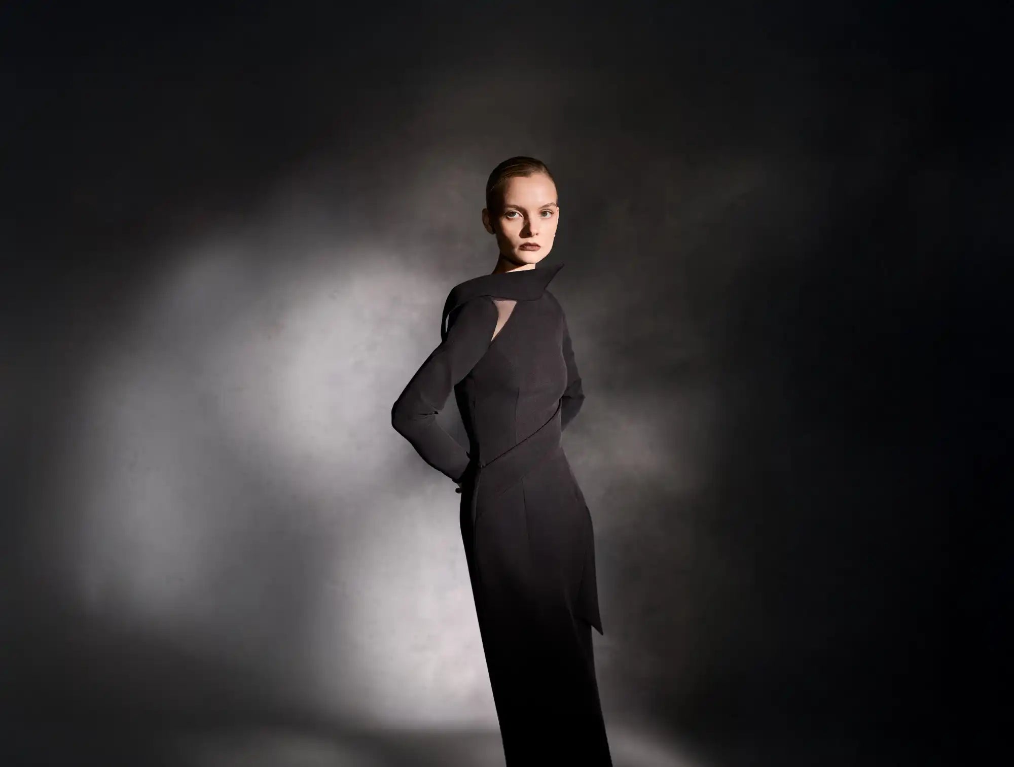 A model wearing a black, long-sleeved dress with an asymmetrical neckline and a cutout detail.
