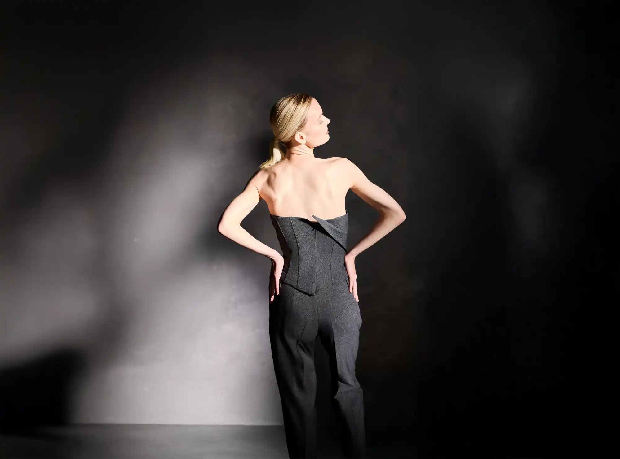 A slender woman in a strapless black jumpsuit with a structured bodice.