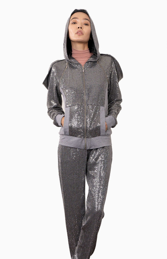 Elegant, silver, futuristic, sequin hoodie with an oversized, lined hood, decorative zippers and draped shoulders. Worn over matching silver sequin joggers
