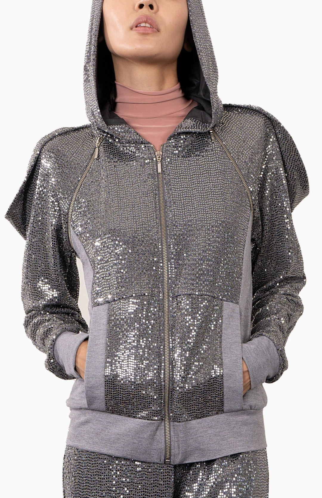 Designer,  silver, futuristic, sequin hoodie with an oversized, lined hood, decorative zippers and draped shoulders. Worn over matching silver sequin joggers