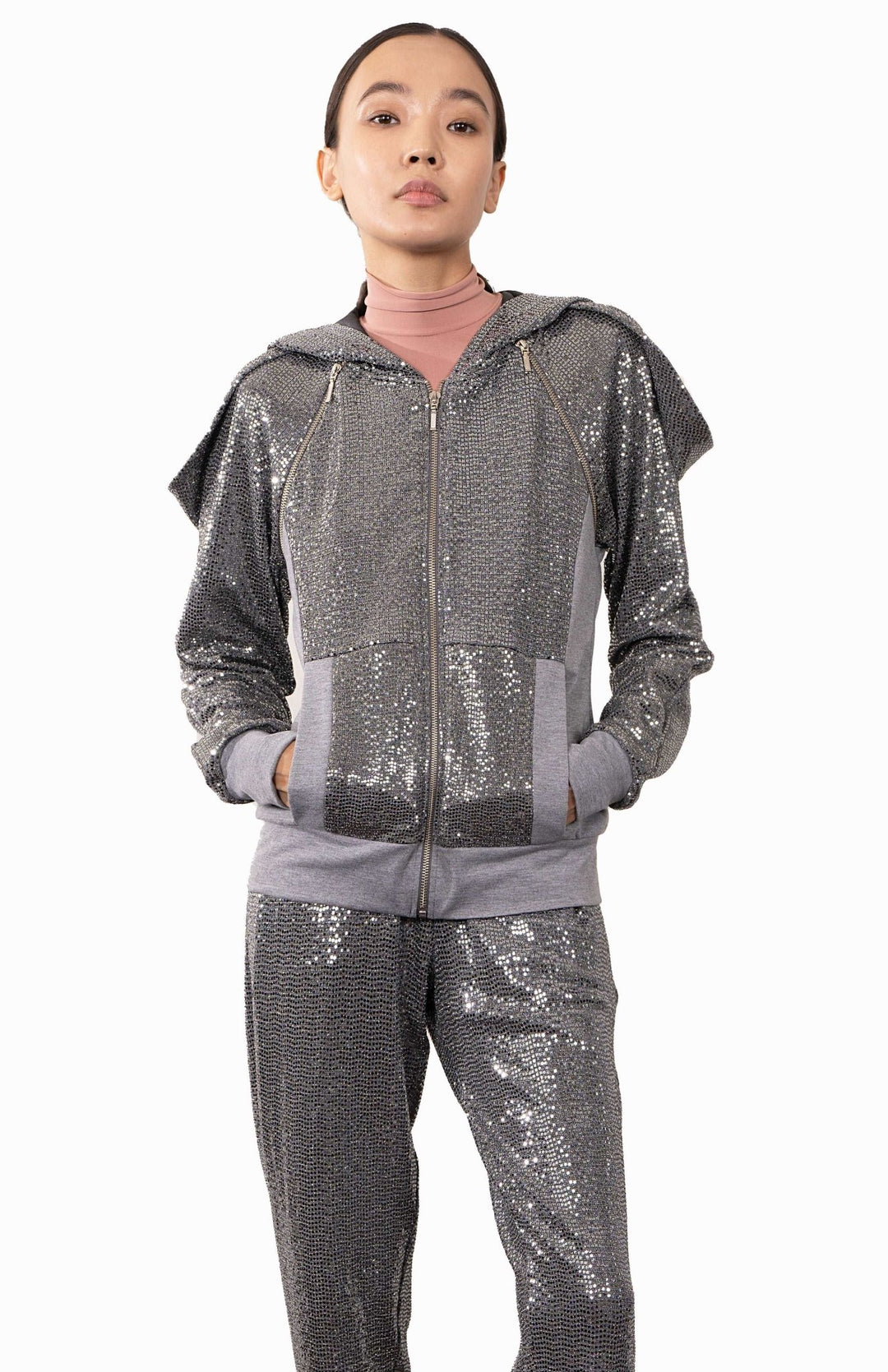 Chic, silver, futuristic, sequin hoodie with an oversized, lined hood, decorative zippers and draped shoulders. Worn over matching silver sequin joggers