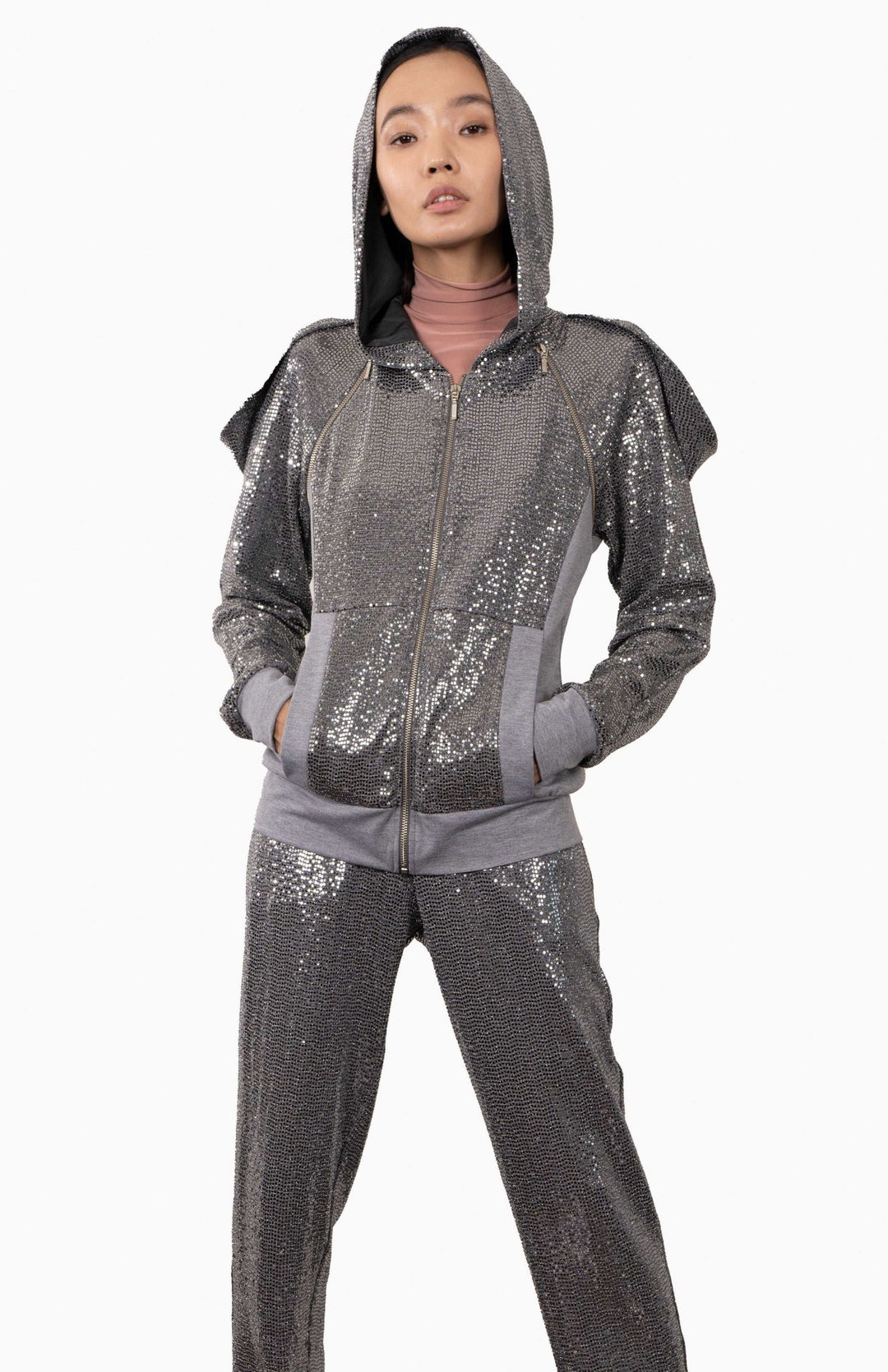 Silver, futuristic, sequin hoodie with an oversized, lined hood, decorative zippers and draped shoulders. Worn over matching silver sequin joggers